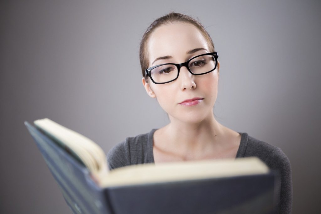 Mulher branca, com ôculos, lendo livro: preparar para concurso público